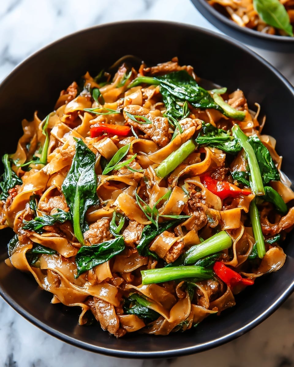 A black bowl filled with a stir-fry of wide, flat brown noodles layered with chunks of cooked brown meat, bright green leafy vegetables, and small pieces of red bell pepper, all coated in a shiny sauce. The noodles form the main base layer, with meat and vegetables spread evenly on top and mixed throughout. Some green herbs are scattered over the top for garnish. The bowl sits on a white marbled surface with part of a second dish blurred in the upper right corner photo taken with an iphone --ar 4:5 --v 7