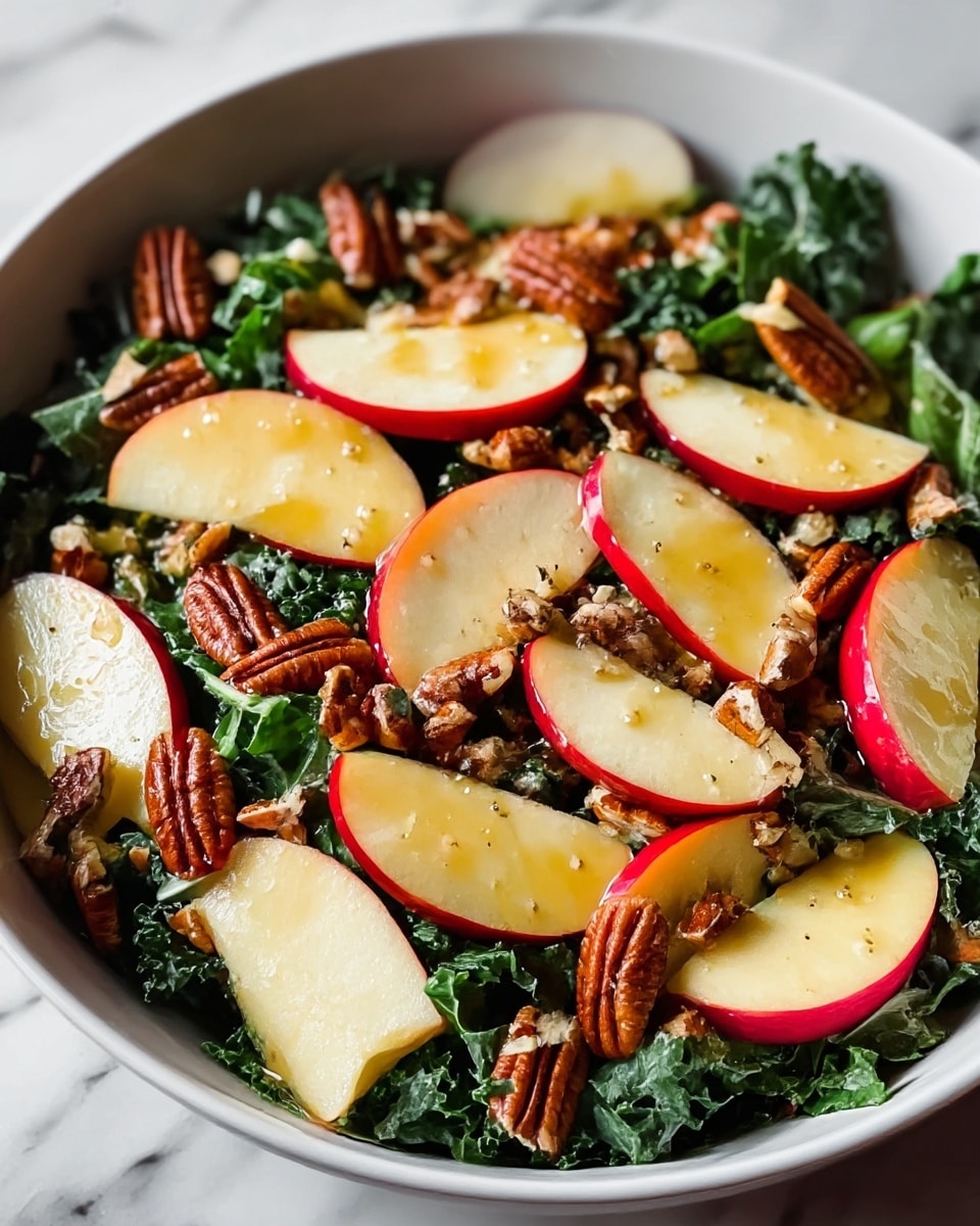 A white bowl is filled with a fresh salad showing three main layers: the bottom layer has dark green leafy kale with a slightly rough texture, the middle layer has many slices of red apple with white inside and smooth skin, placed all over the kale, and the top layer is scattered with small, brown pecan halves and pieces that look crunchy. The salad looks lightly dressed with a shiny honey-colored dressing sparkling over the apple slices and nuts. The bowl is placed on a white marbled surface. photo taken with an iphone --ar 4:5 --v 7