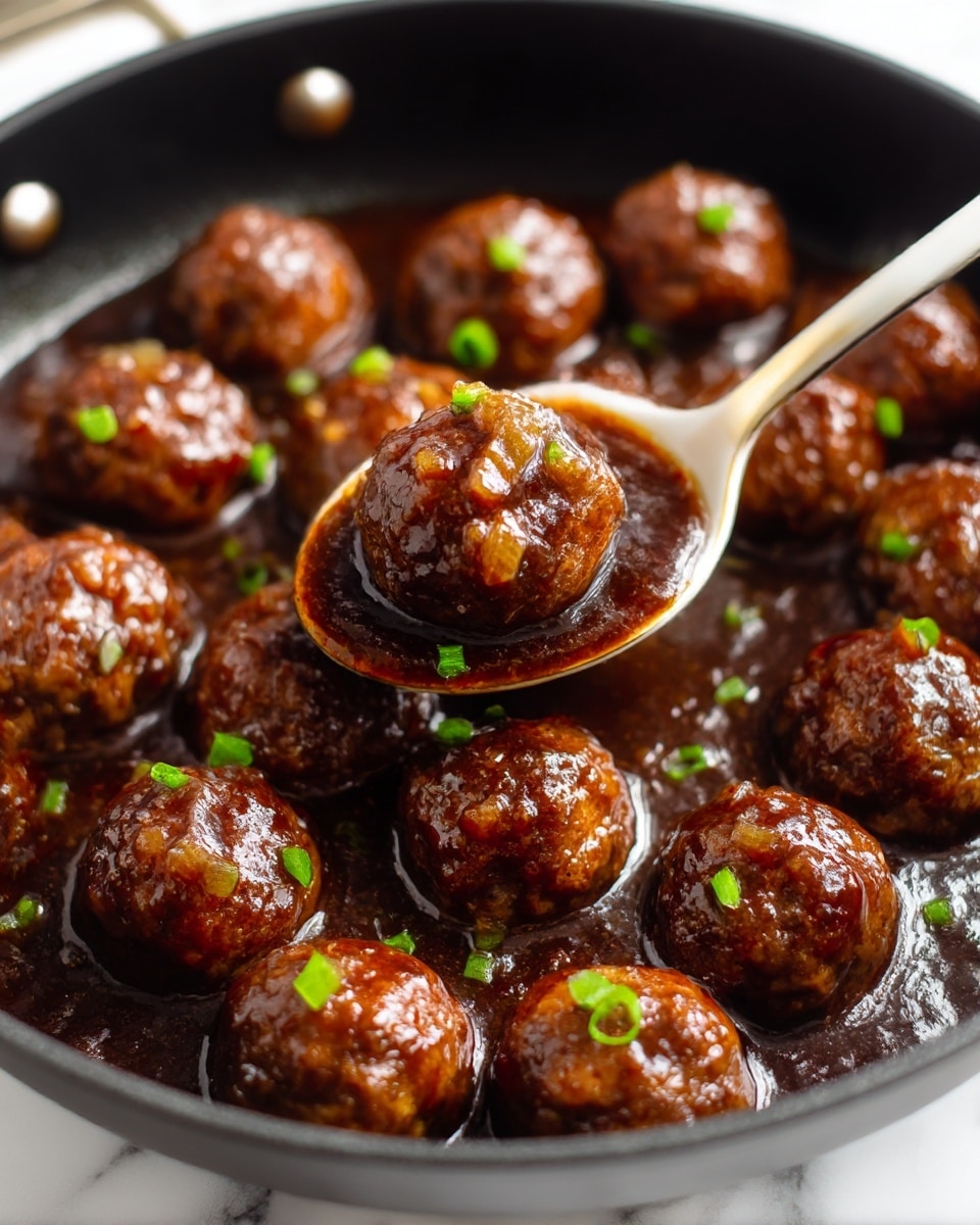 A close-up view of a black pan filled with about fifteen shiny, brown meatballs covered in a thick, dark brown sauce with visible small chunks of cooked onion on top. The meatballs are round and firm, sitting close together, and sprinkled with small pieces of bright green chopped scallions. A white and gold spoon lifts a single meatball from the pan, showing the sauce glistening over its surface. The background is a white marbled texture. photo taken with an iphone --ar 4:5 --v 7
