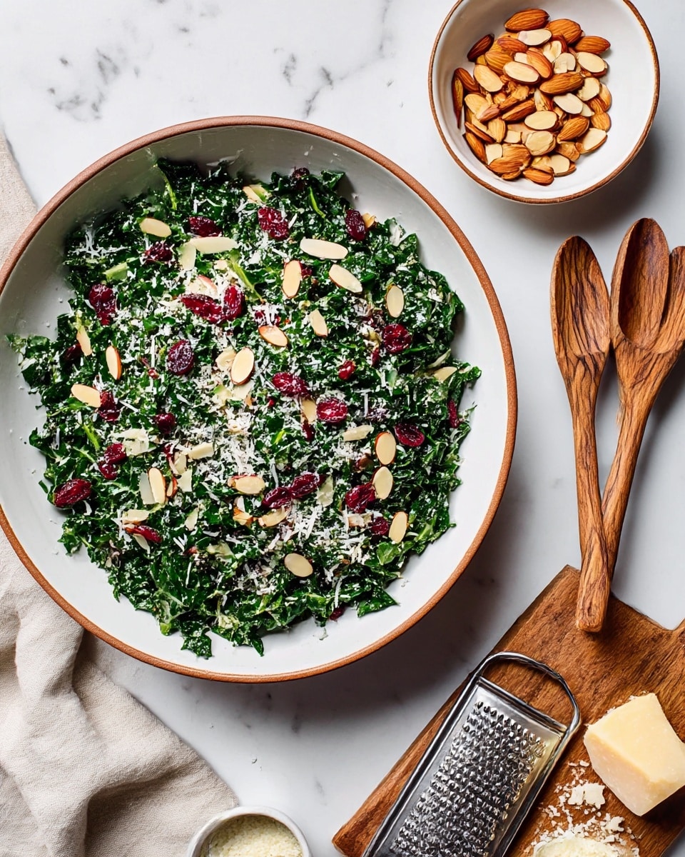 A large white bowl with a brown rim holds a fresh kale salad made of finely chopped dark green kale leaves mixed with bright red dried cranberries and light beige sliced almonds scattered on top. The salad is lightly sprinkled with white shredded cheese. Next to the bowl, there is a smaller white bowl with a brown rim filled with more sliced almonds. On the right side, a white plate holds wooden salad tongs with visible grain texture. In the lower right corner, a wooden cutting board contains a metal grater, a piece of parmesan cheese, and a small white bowl with grated cheese. The whole scene is set on a white marbled surface with a beige cloth napkin partially visible on the left side. photo taken with an iphone --ar 4:5 --v 7