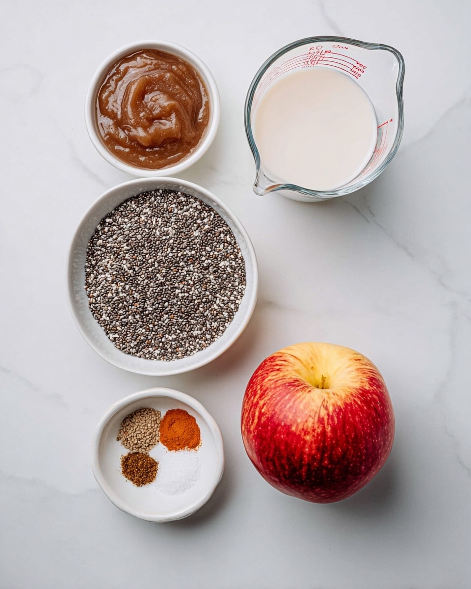The image shows five ingredients arranged neatly on a white marbled surface. At the center is a bowl filled with many tiny black and white chia seeds, forming a textured mound. To the top right of the chia seeds, there is a clear glass measuring cup filled with white milk, showing red measurement markings on its side. To the bottom right, a whole red and yellow apple with smooth skin sits on the surface. To the top left of the chia seeds, a white bowl contains thick, smooth, dark brown apple sauce with a glossy finish. Below the apple sauce, a smaller white bowl holds four small piles of dry spices and salt, featuring different shades of brown, orange, and white, arranged side by side. The scene has soft, even lighting highlighting the textures and colors, photo taken with an iphone --ar 4:5 --v 7