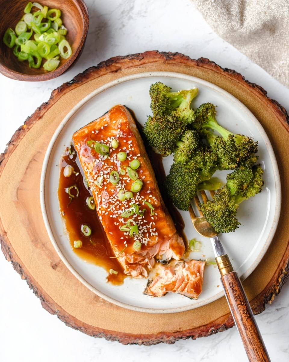 A white round plate on a wooden slice holds a salmon fillet broken at the bottom to show its pink, flaky inside. The top of the salmon is glazed a shiny reddish-brown and sprinkled with white sesame seeds and green sliced scallions. To the right of the salmon, there are several crisp, bright green broccoli florets sitting in a dark brown sauce. A fork with a wooden handle lies on the plate near the broccoli. In the top left, there is a small brown bowl filled with green sliced scallions, all placed on a white marbled surface. photo taken with an iphone --ar 4:5 --v 7