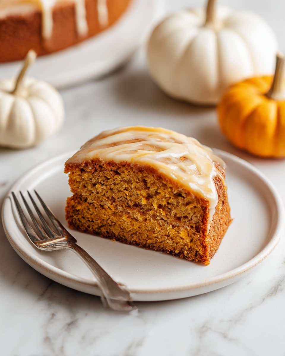 A thick square slice of orange-brown pumpkin cake with a moist, crumbly texture sits on a white plate. The top of the cake has a few streaks of light tan glaze that looks smooth and slightly shiny. The cake has one visible layer, and it appears soft and dense. A silver fork rests beside the cake on the plate. In the background, there are whole white and small yellow pumpkins slightly out of focus, all set on a white marbled surface. photo taken with an iphone --ar 4:5 --v 7