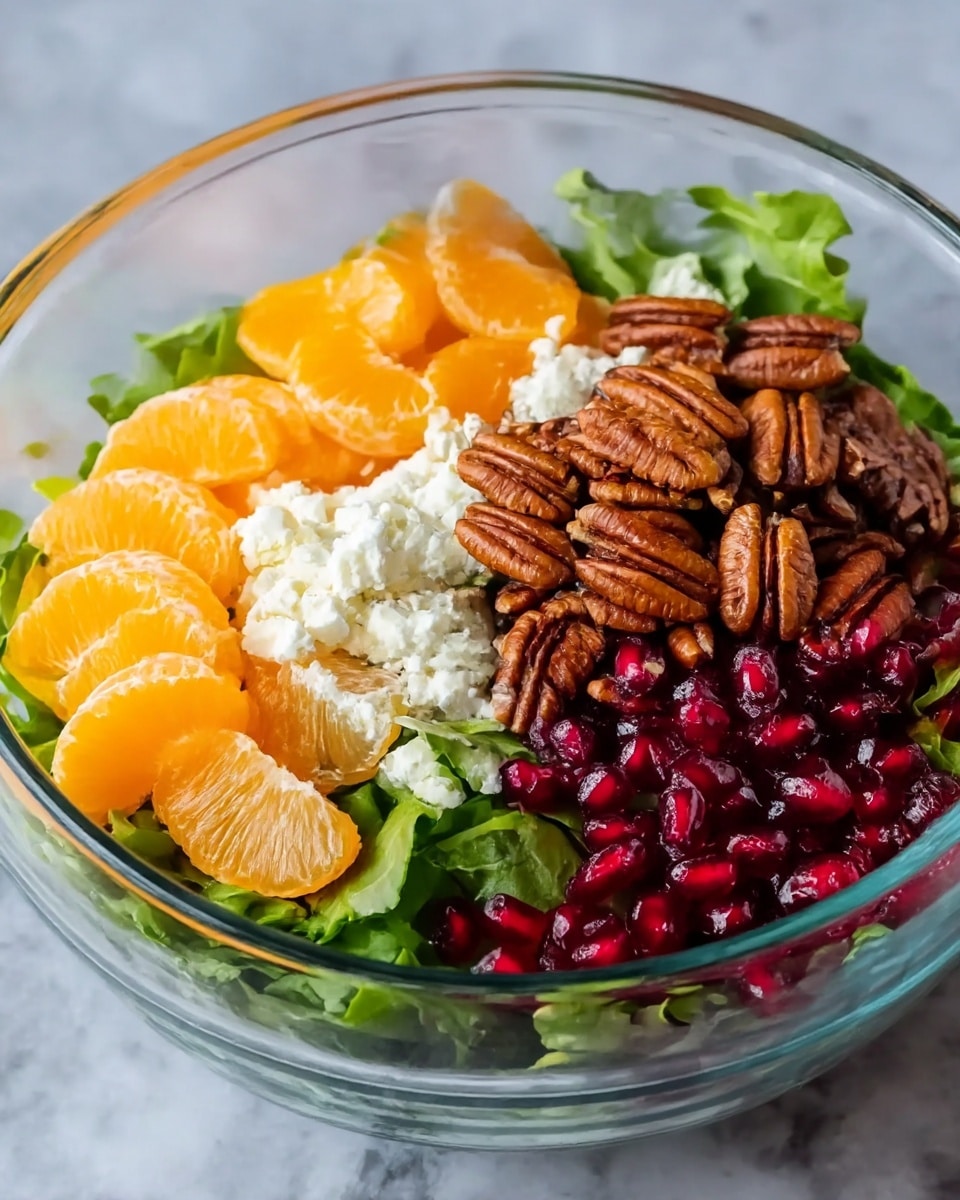 A clear glass bowl filled with a fresh salad, layered with bright green leafy mixed greens at the bottom. On top, there are four distinct sections: shiny, bright orange mandarin slices on the left, white crumbly cheese in the upper middle, toasted brown pecan halves piled in the upper right, and deep red pomegranate seeds to the lower right. The bowl sits on a white marbled textured surface. photo taken with an iphone --ar 4:5 --v 7
