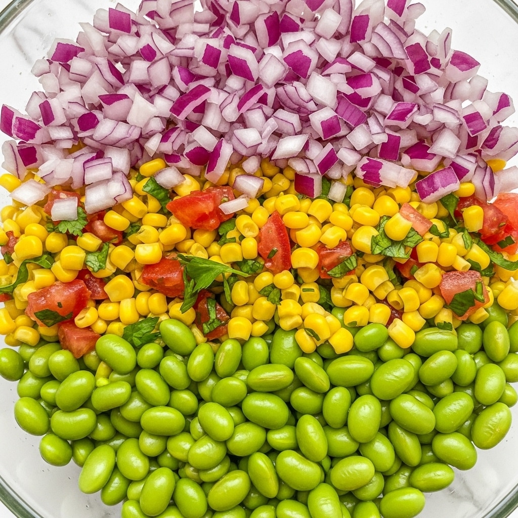 A close-up view of a colorful salad in a clear bowl with a white marbled background, featuring three main layers: the bottom layer is bright green edamame beans, the middle layer consists of yellow corn kernels mixed with diced red tomatoes and small pieces of green cilantro, and the top layer shows finely chopped red onions scattered evenly across, with the mixture looking fresh and slightly shiny. photo taken with an iphone --ar 4:5 --v 7