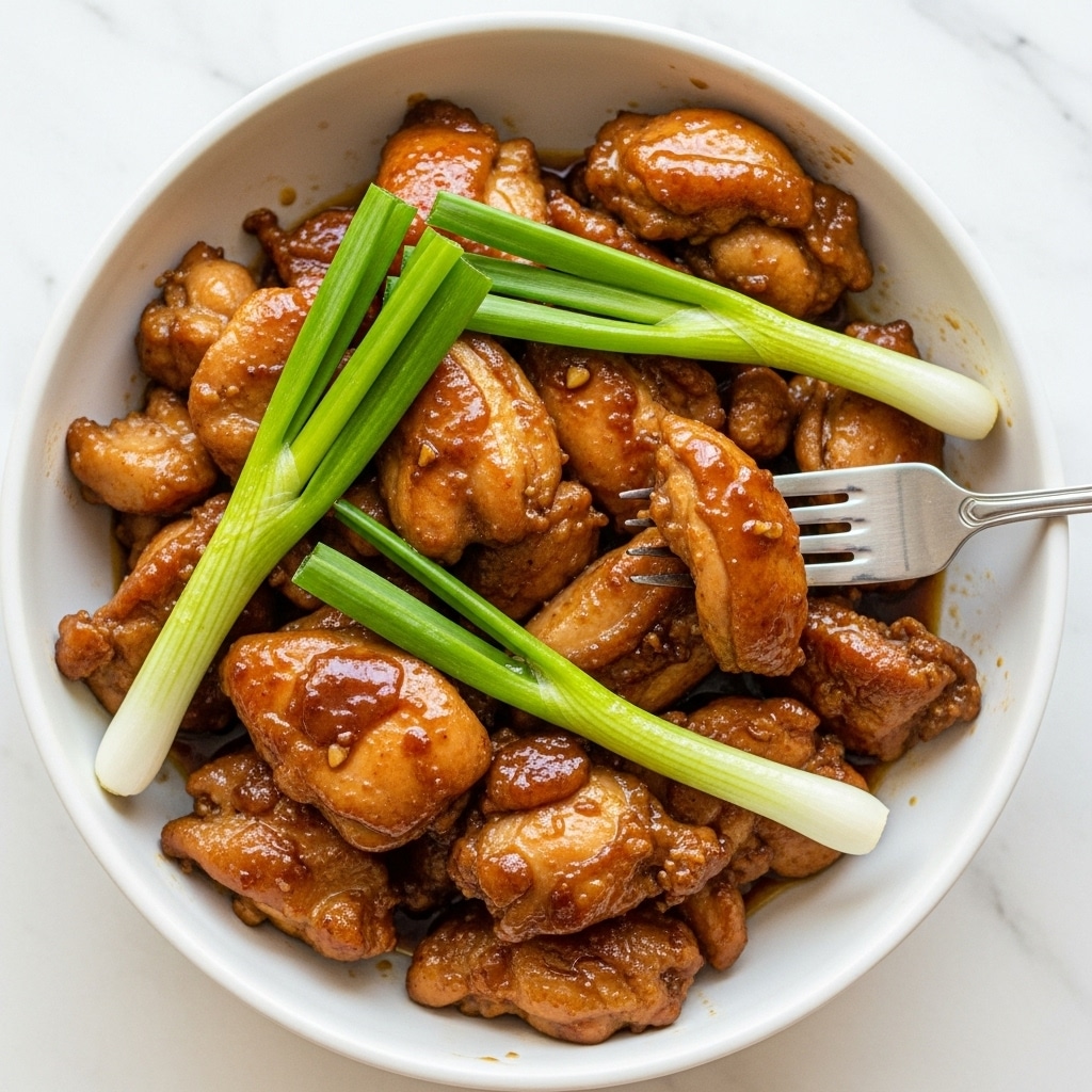 The image shows a close-up of a white bowl filled with brown, glazed pieces of cooked chicken. The chicken looks tender with shiny, slightly oily surfaces. Inside the bowl, there are green onion stalks placed among the chicken, adding a fresh green contrast. A silver fork is inserted into one chicken piece on the right side, and the bowl is set on a white marbled background. The dish looks warm and savory, with rich layers of brown meat and light green vegetables. photo taken with an iphone --ar 4:5 --v 7