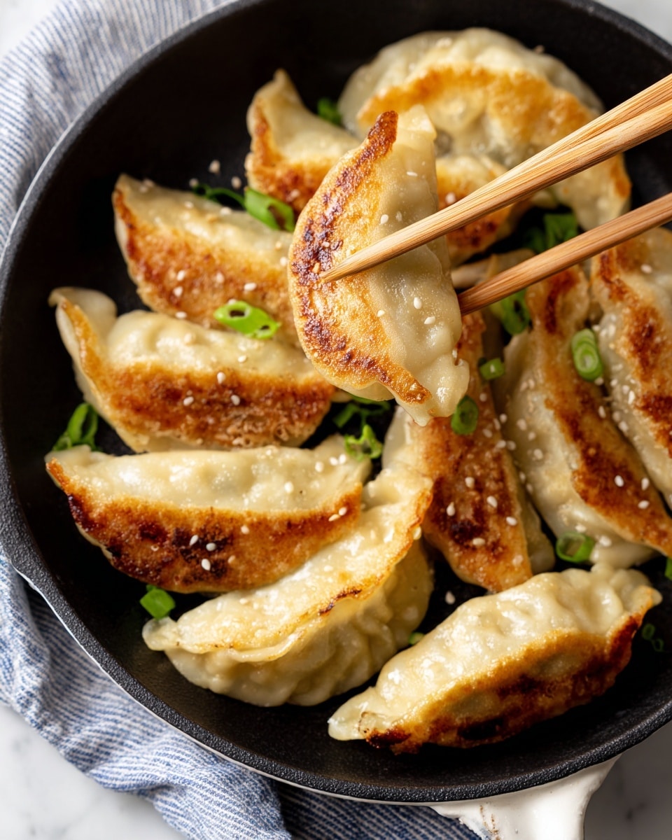 A close-up image of a golden brown fried dumpling held by a pair of wooden chopsticks above a black pan filled with several more dumplings. Each dumpling is plump with a smooth, slightly shiny dough surface and browned crispy bottom layers, showing a crunchy texture. The dumplings are arranged loosely in the pan, with small green onion slices and sesame seeds scattered on top, adding specks of green and white. The pan is set on a white marbled surface with a blue and white striped cloth partially visible. photo taken with an iphone --ar 4:5 --v 7