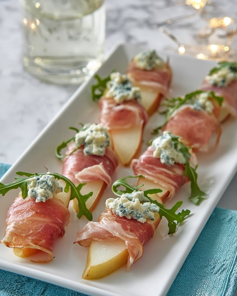 The image shows a rectangular white plate holding six pieces of slices of pear, each piece wrapped in thin pink prosciutto slices. On top of each pear slice is a dollop of blue cheese with white and blue-green marbling. Small green arugula leaves are placed between and on the pear and prosciutto layers, adding a fresh touch. The plate sits on a white marbled surface with some blurred clear glasses in the background. photo taken with an iphone --ar 4:5 --v 7