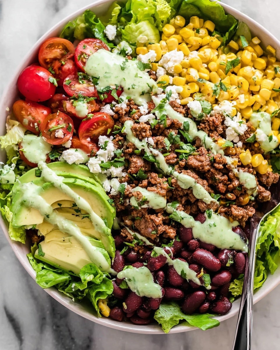 This dish is a layered salad served in a white bowl. The bottom layer is fresh green lettuce leaves spread across the bowl. On top, there are sections of bright yellow corn, red cherry tomatoes (some halved), and dark red kidney beans all around the edges. In the center is a generous portion of cooked ground beef mixed with small bits of caramelized onions. Thin slices of avocado are placed on one side. The entire dish is sprinkled with crumbled white cheese and chopped fresh green herbs. A light green creamy dressing is drizzled over all the layers, adding a smooth texture and color contrast. A silver spoon with a black handle rests inside the bowl on a white marbled surface. Photo taken with an iphone --ar 4:5 --v 7
