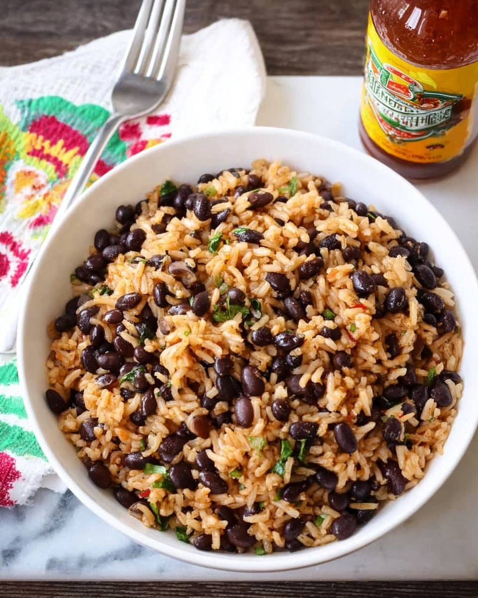 A white bowl filled with a mixed dish of light brown rice and shiny black beans, speckled with small green herb pieces and finely chopped onions, creating a texture of soft grains and beans. The bowl sits on a white marbled surface with a colorful beige cloth napkin to the left, topped with a silver fork. Behind the bowl, there is a bottle with a yellow and red label. photo taken with an iphone --ar 4:5 --v 7