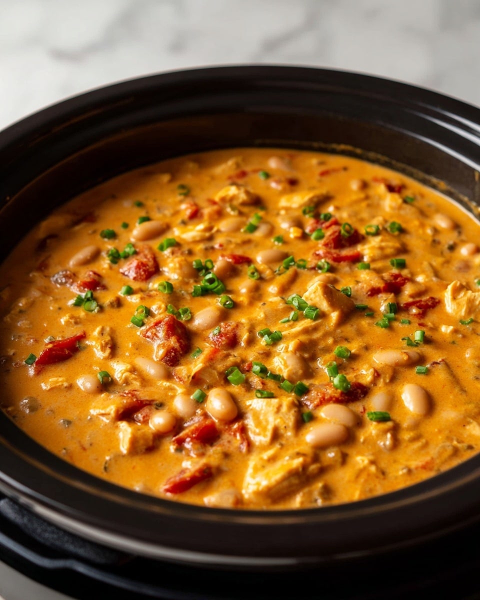 A thick orange creamy stew fills a black pot, showing layers of small white beans, chunks of light brown chicken, and red tomato pieces evenly mixed throughout. The stew has small green onion slices sprinkled on top, adding a fresh touch to the rich, smooth texture and warm color. The pot sits on a white marbled surface, focusing on the stew’s hearty and inviting appearance. photo taken with an iphone --ar 4:5 --v 7