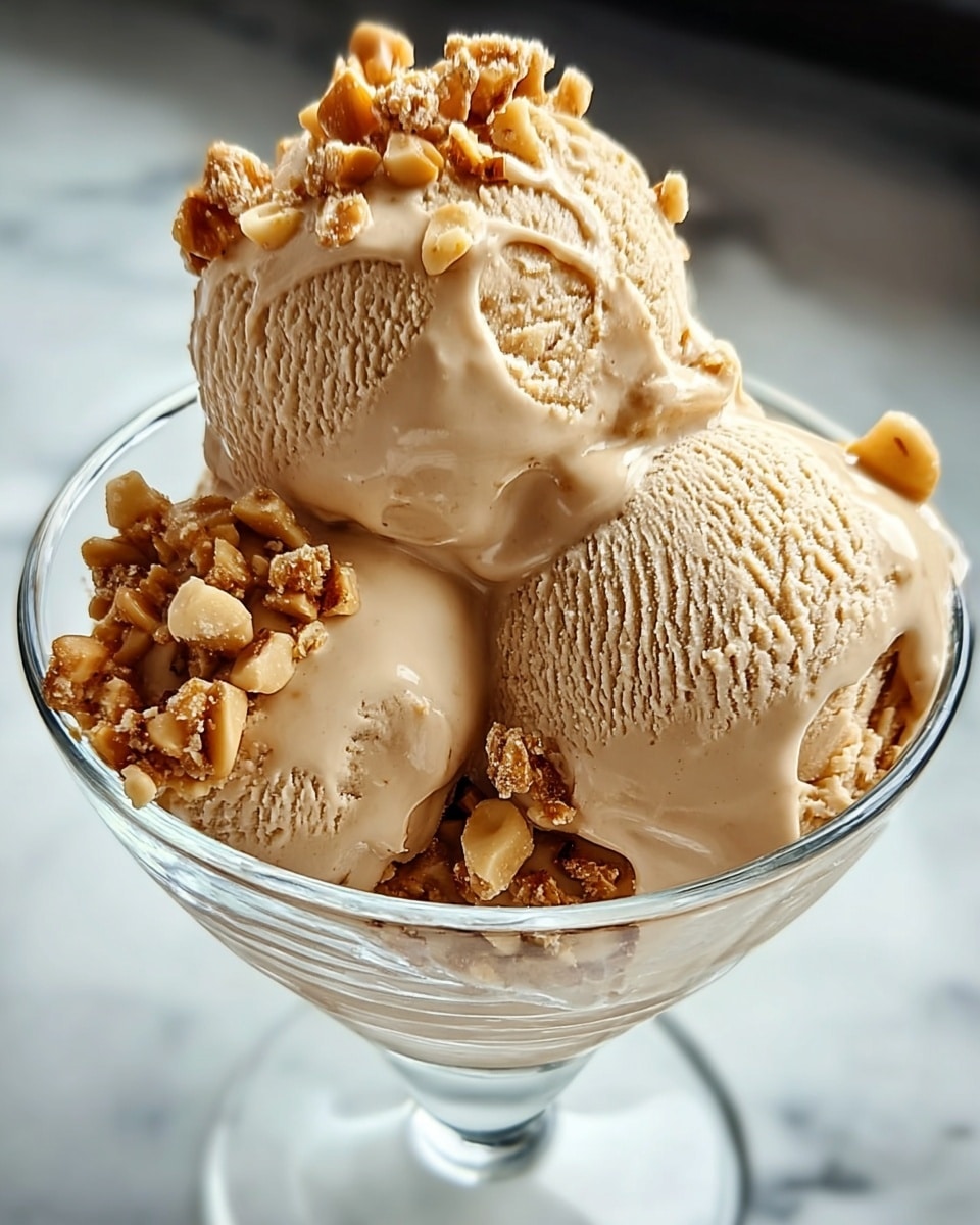 The image shows a glass dessert bowl filled with three scoops of light brown ice cream, each scoop smooth with visible creamy texture and soft ridges. Small chunks of crunchy caramel-colored nuts are sprinkled on and around the scoops, adding a contrasting texture and a warm color. The bowl is clear, sitting on a white marbled surface. The soft light highlights the creamy surface and nut pieces, making the ice cream look rich and inviting. photo taken with an iphone --ar 4:5 --v 7