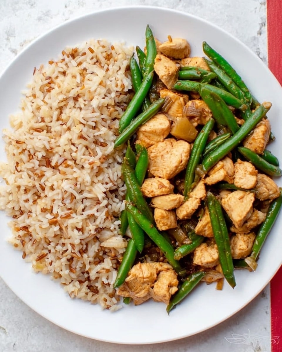 A white plate with two main parts: on the left side, a mix of cooked rice with a light beige and brown color, showing some grain texture and slight fluffiness; on the right side, cooked green beans with a shiny, smooth green surface mixed with small chunks of cooked chicken that are light golden brown with a soft texture; the green beans and chicken are placed on top and blend together slightly but mostly stay separate from the rice. The plate is on a white marbled surface with a slight red section visible on the right edge. Photo taken with an iphone --ar 4:5 --v 7