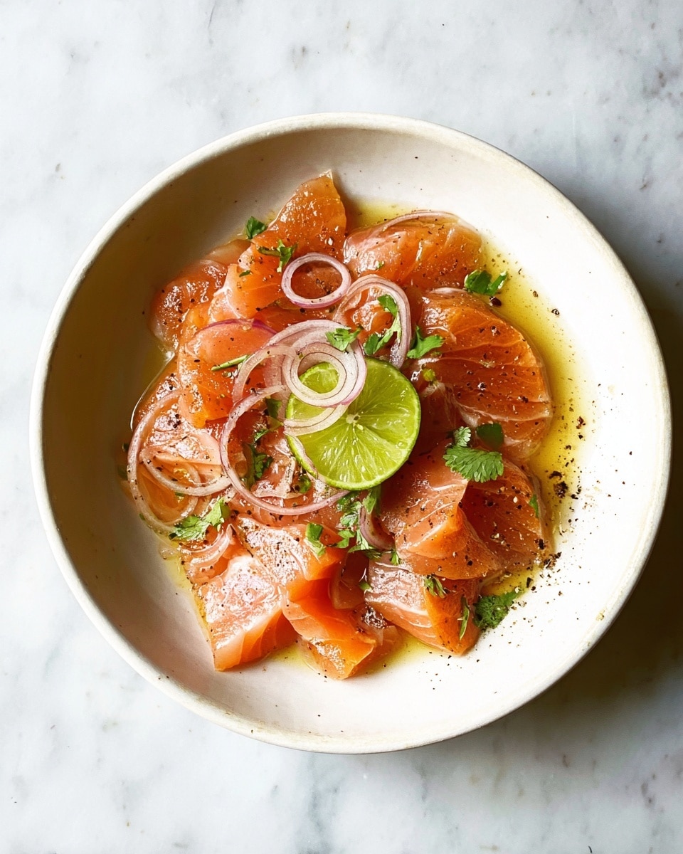 A white bowl holds several thin slices of raw salmon, arranged in a loose overlapping circle, showing their bright orange-pink color with smooth texture and subtle white marbling. On top of the salmon are thin rings of pale pink shallots and small green cilantro leaves scattered around. In the center, there is a partly squeezed lime wedge with vibrant green skin and pale juicy inside. The dish is lightly coated with a shiny, golden oil or sauce that pools at the bottom, and small bits of ground black pepper are sprinkled on the salmon, adding dark specks. The bowl rests on a white marbled surface. Photo taken with an iphone --ar 4:5 --v 7
